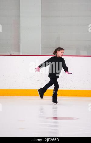 Das kleine Mädchen trainiert Eiskunstlauf auf der Eishalle. Stockfoto