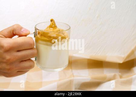 Den Dalgona-Kaffee in einem durchsichtigen Kaffeebecher peitschten. Koreanisches Getränkekonzept. Selektiver Fokus. Speicherplatz kopieren Stockfoto