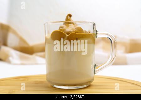 Den Dalgona-Kaffee in einem durchsichtigen Kaffeebecher peitschten. Koreanisches Getränkekonzept. Selektiver Fokus Stockfoto