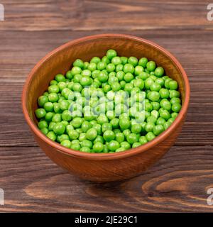 Frische grüne Erbsen in einer Schüssel aus der Nähe auf einem braunen Holztisch. Stockfoto