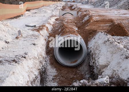 Verlegung der Abflussleitung aus Stahlbeton zwischen großen Wohngebieten. Neue Sanitäranlagen, Sturmabflusssysteme auf der Baustelle. Stockfoto