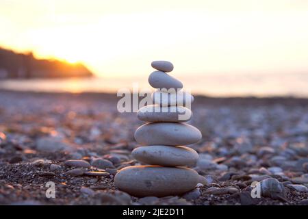 Steinpyramide am Strand. Perfekte Balance aus Kieselsteinen am Meer gegen Sonnenuntergang. Konzept von Balance, Harmonie und Meditation. Jemandem beim Wachsen oder Aufsteigen helfen oder unterstützen. Stockfoto