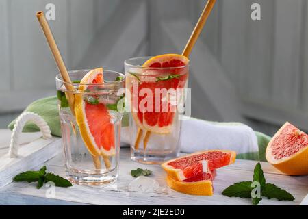 Erfrischende Cocktails im Sommer mit Grapefruitscheiben und Minze auf einem weißen Holztablett Stockfoto