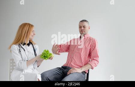 Der männliche Patient verweigert gesunde Nahrung, die von einem Ernährungsberater angeboten wird. Gesunde Pflanzennahrung Diätetik. Stockfoto