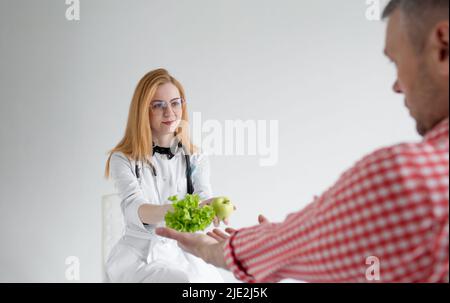 Eine Ernährungswissenschaftlerin reicht einem männlichen Patienten Gemüse und Obst aus. Das Konzept der richtigen und gesunden Ernährung Stockfoto