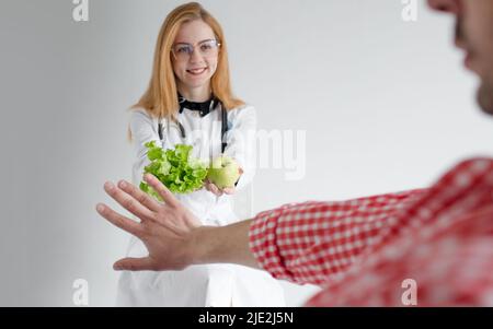 Ein Mann ignoriert den Vorschlag eines Ernährungswissenschaftlerin Gemüse Obst Übergang zu gesunden und gesunden Lebensmitteln. Ablehnung des Vegetarismus Stockfoto