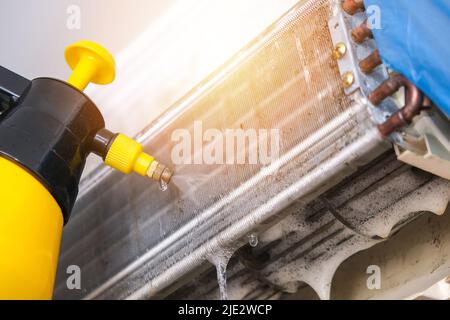 Ein Mann wäscht einen speziellen Schaum ab, um Klimaanlagen mit einem Wasserstrahl unter Druck zu reinigen. Wartung des geteilten Systems. Stockfoto