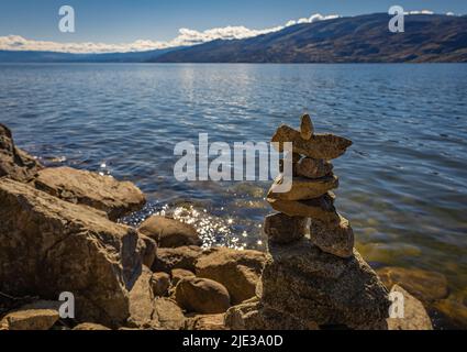 Blick auf einen Inukshuk vor einem Sommersee. Inushuk steht auf einem Felsen im Kelowna Okanagan Lake BC. Ein Inuksuk ist ein von Menschen gemachtes Wahrzeichen aus Stein. Reise Stockfoto