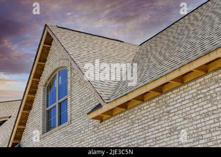 Ein neues Haus wird mit Asphaltschindeln und Abdichtung für die Eckdachschindeln gebaut Stockfoto