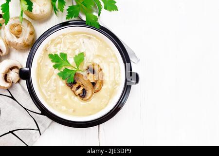 Suppenpüree aus Champignons, Kartoffeln, Zwiebeln und Rahm in einer Schüssel, einem Küchentuch, Petersilie und einem Löffel auf hellem Holzbrett Hintergrund von oben Stockfoto