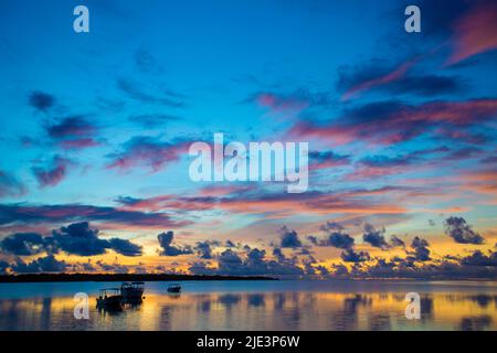 Der Himmel leuchtet im Morgengrauen mit Booten, die auf stillen Gewässern vor der Insel Yap, Mikronesien, schwimmen. Stockfoto