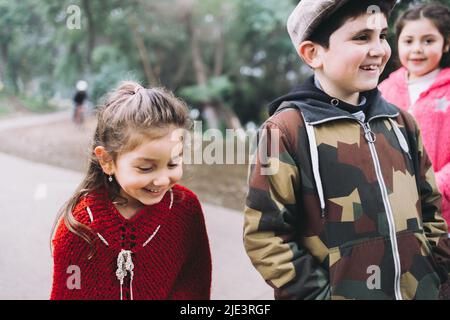 Drei Kinder, zwei Mädchen und ein Junge, die in einer Parkstraße spazieren und sich unterhalten. Stockfoto