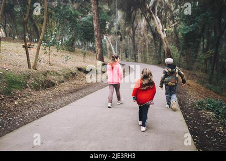 Drei Kinder, zwei Mädchen und ein Junge, die in einer Parkstraße spazieren und sich unterhalten. Stockfoto