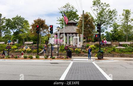 BLOWING ROCK, NC, USA-20 JUNE 2022: Junge Frau wartet auf die Straße vor dem Stadtpark. Paare auf Bänken und Blumenbeeten im Hintergrund. Stockfoto