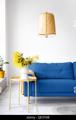 Vase mit Mimosenblumen auf dem Tisch und blauem Sofa im hellen Wohnzimmer Stockfoto