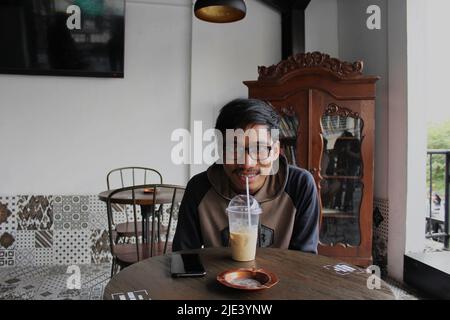 Yogyakarta, Indonesien - 08 07 2019: Ein glücklicher Ausdruck eines Mannes, der während seines Urlaubs in Yogyakarta, Zentraljava, ein kaltes Glas Kaffee genießt Stockfoto
