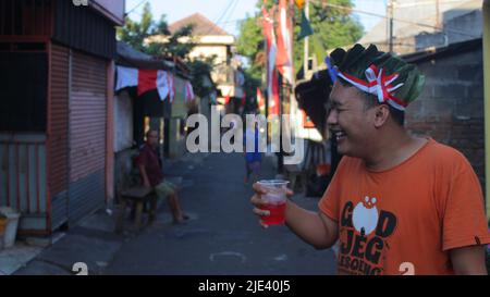 Jakarta, Indonesien - 08 18 2019: Ausdruck eines glücklichen Mannes, der ein Glas Getränk in der Hand hält, während er an der indonesischen Jubiläumsparade 72. teilnimmt Stockfoto