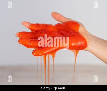 Roter Schleim, der aus der Hand einer Frau auf einem weißen Hintergrund herabfließt. Stockfoto