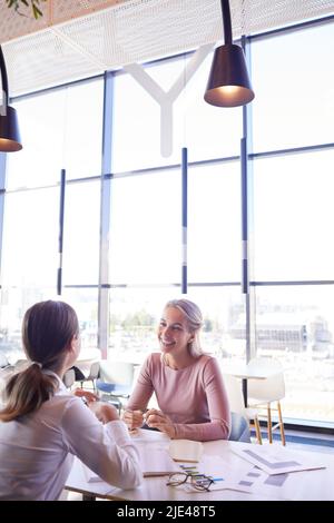 Positive, attraktive junge Finanzanalysten sitzen mit statistischen Datenpapieren an einem Tisch und arbeiten gemeinsam an einem Geschäftsbericht Stockfoto