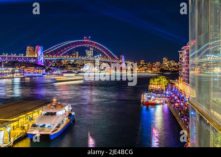 Spiegelung der Sydney Harbour Bridge in der Glaswand des Circular Quay-Bereichs über den Fähranlegestellen für Passagiere beim Vivid Sydney Light Show Festival. Stockfoto