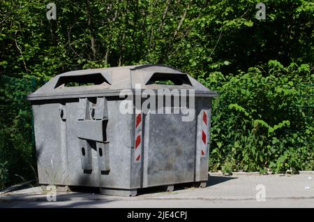 Papierrecycling-Sammelstelle / leere Papierbank / großer Müllcontainer aus Stahl mit Reflektoren, die auf einer Straße mit Bäumen im Hintergrund stehen Stockfoto