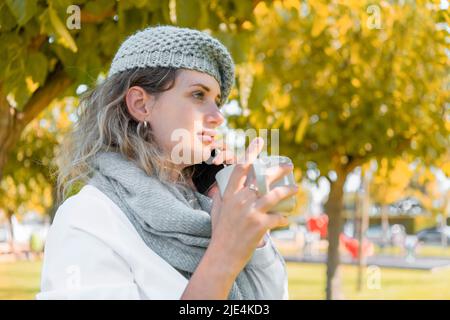 Junge Frau mit einem Wollhut, die ihrem Telefon zuhört Stockfoto