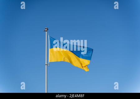 Ukrainische Flagge mit gelb-blauen Farben auf dem Hintergrund des klaren blauen Himmels. Stockfoto