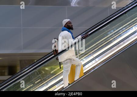 Afroamerikanischer Passagiermann mit Koffer steht auf Rolltreppe, hält Handlauf im Flughafenterminal Stockfoto