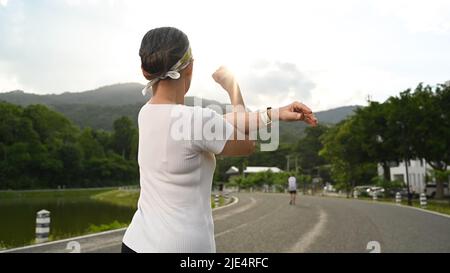 Rückansicht Dame mittleren Alters wärmt sich auf und streckt ihre Arme vor dem morgendlichen Training. Fitness, Sport und gesundes Lifestyle-Konzept Stockfoto