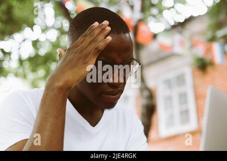 Erschöpfter, gestresster, multirassischer Mann mit dunkler Haut in einer Brille, der die Hände am Kopf hielt, litt und die Augen vermasselte Stockfoto
