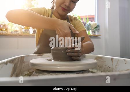 Zugeschnittenes Bild einer Keramikerin, die in einer kreativen Atelierwerkstatt handwerkliches Geschirr auf dem Töpferrad kreiert Stockfoto