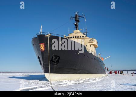 Rovaniemi, Finnland - 21.. März 2022: Sampo, ein Eisbrecher-Schiff, vor Anker auf der gefrorenen ostsee, an einem sonnigen Wintertag, Touristen im Flotationsanzug Stockfoto