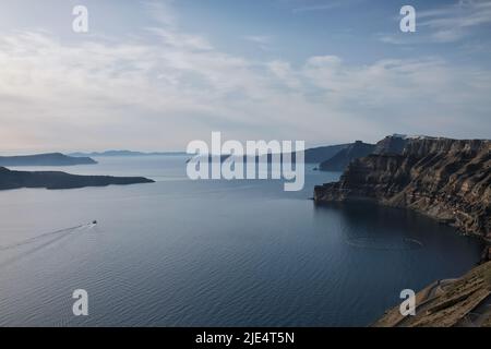 Atemberaubende Aussicht auf Fira, Oia, den Vulkan und ein kleines Boot, das den Hafen von Athinios in Santorini Griechenland verlässt Stockfoto