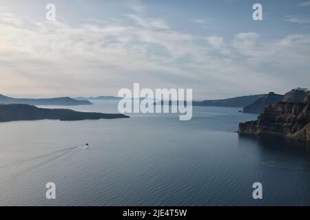 Atemberaubende Aussicht auf Fira, Oia, den Vulkan und ein kleines Boot, das den Hafen von Athinios in Santorini Griechenland verlässt Stockfoto