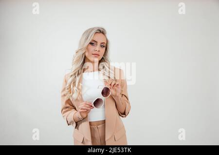 Junge schöne Frau, Geschäftsdame mit Sonnenbrille in beigem Anzug auf weißem Hintergrund Studioaufnahme. Optik-Konzept Stockfoto