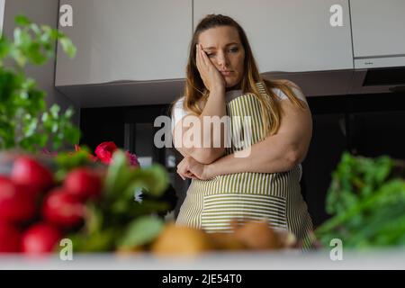 Müde, traurig und gelangweilt plus Größe blonde Frau hält Kopf in der Hand, denken, was zu kochen, haben keine Ahnung. Suche nach Rezept Stockfoto