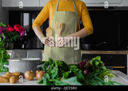 Unkenntlich Frau in gestreifte Küchenschürze, setzen Holzspatel Utensil in die Tasche. Weibliche Köchin beginnt zu kochen Stockfoto