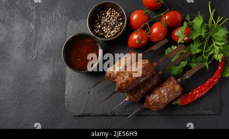 Shish Kebab ist eine beliebte Mahlzeit aus Spieß- und gegrillten Fleischwürfeln. Gerösteter Rinderkebab auf einem Holzspieß mit Gewürzen, Kräutern und Tomaten Stockfoto