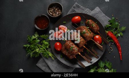 Shish Kebab ist eine beliebte Mahlzeit aus Spieß- und gegrillten Fleischwürfeln. Gerösteter Rinderkebab auf einem Holzspieß mit Gewürzen, Kräutern und Tomaten Stockfoto