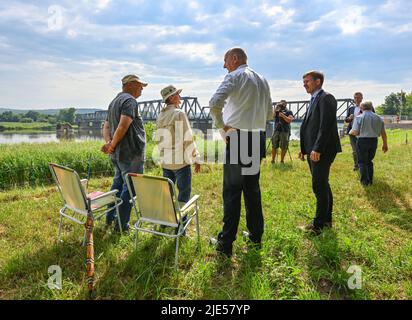 25. Juni 2022, Brandenburg, Neurüdnitz: Dietmar Woidke (M, SPD), Ministerpräsident von Brandenburg, und Karsten Birkholz (r, überparteilich), Kreisdirektor Barnim-Oderbruch, sprechen mit dem Ehepaar Ilona und Rainer Tank über die Öffnung der Europabrücke, die eine Verbindung zwischen den beiden Ländern über die deutsch-polnische Grenzfluß oder schafft. Die ehemalige Eisenbahnbrücke zwischen der brandenburgischen Gemeinde Oderaue (Oderbruch) und der polnischen Stadt Siekierki in Vorpommern, Cedynia, wurde am selben Tag für Fußgänger und Radfahrer geöffnet. Mietwagen können diese Verbindung nicht verwenden. Das Europabr Stockfoto