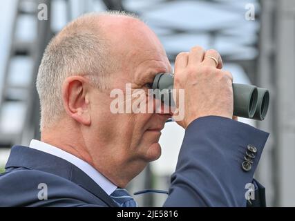 25. Juni 2022, Brandenburg, Neurüdnitz: Der Ministerpräsident von Brandenburg, Dietmar Woidke (SPD), blickt durch ein Fernglas und sieht in der Nähe der Brücke bei der Öffnung der Europabrücke, die eine Verbindung zwischen den beiden Ländern über die deutsch-polnische Grenzfluß oder bietet, eine Adlereule. Die ehemalige Eisenbahnbrücke zwischen der brandenburgischen Gemeinde Oderaue (Oderbruch) und der polnischen Stadt Siekierki in Vorpommern, Cedynia, wurde am selben Tag für Fußgänger und Radfahrer geöffnet. Mietwagen können diese Verbindung nicht verwenden. Die Europabrücke schafft eine weitere Möglichkeit, die oder Riv zu überqueren Stockfoto