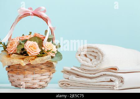 Weiße Bettwäsche Bettwäsche Rolltücher Korb mit Blumen auf dem Tisch auf blauem Hintergrund. Stockfoto