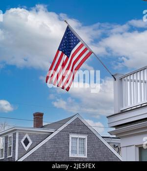 Vereinigte Staaten von Amerika Flagge gegen blauen Himmel mit Wolken, die an der Stange an der weißen Deckgeländer auf dem Dach des Hauses auf Cape Cod hängen Stockfoto