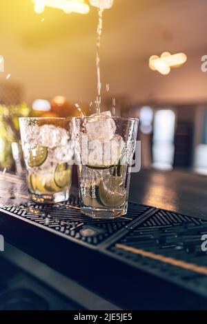 Der Barkeeper macht auf der Theke einen Cocktail auf Wodka-Basis mit Eis und Limette Stockfoto