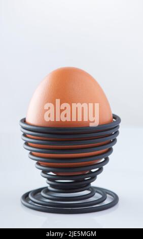 Ein gekochtes Ei in einer spiralförmigen schwarzen Metallstütze, isoliert auf weißem Hintergrund Stockfoto