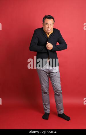 Der asiatische Mann mittleren Alters, der auf dem roten Hintergrund steht. Stockfoto