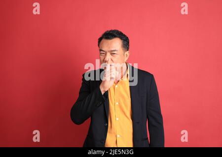 Der asiatische Mann mittleren Alters, der auf dem roten Hintergrund steht. Stockfoto