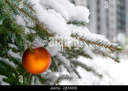 Weihnachtsspielzeug orange Kugel auf dem Weihnachtsbaum. Schnee auf einem Ast. Straßendekoration im Winter. Winterhintergrund. Stockfoto