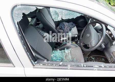 Ein Auto mit der Fahrerseite wurde zerschlagen, nachdem es von einem Dieb angegriffen wurde. Auf den Sitzen im unsicheren Fahrzeug ist ein zerbrochenes Glas aus dem Fenster zu sehen Stockfoto