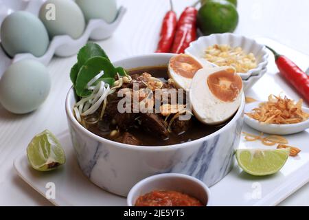 Rawon, Schwarzes Suppengericht Mit Indonesischem Rindfleisch. Schwarze Farbe aus Keluak Nuss als Hauptgewürze, verleiht der Suppe dunkle Farbe und nussigen Geschmack. Stockfoto